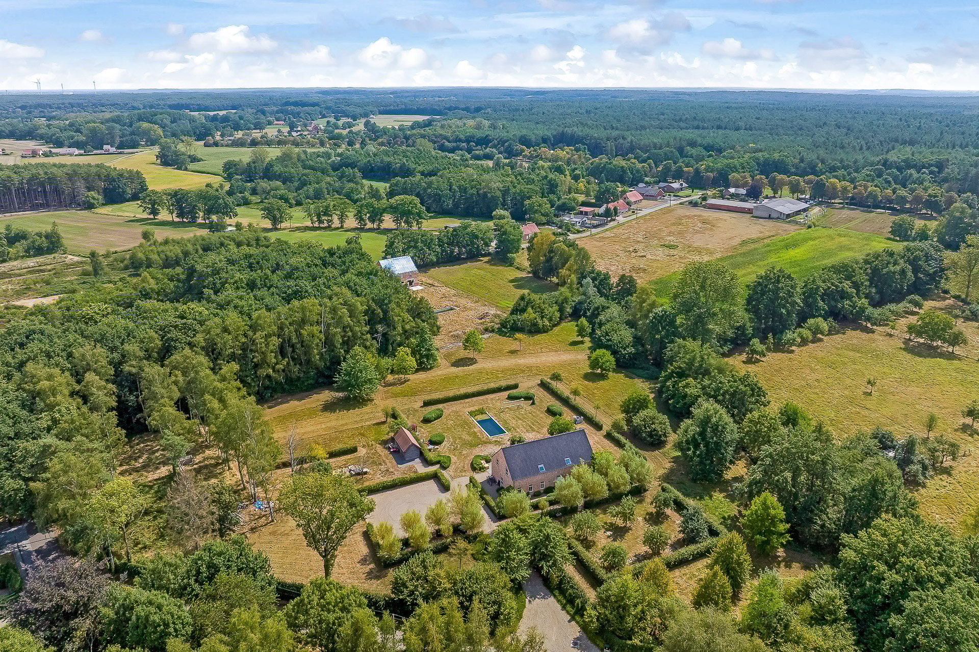 Luchtfoto van een landelijke woning in een bosrijke omgeving, waarbij het volledige perceel, de tuin met zwembad en de groene ligging via dronefotografie in kaart zijn gebracht.