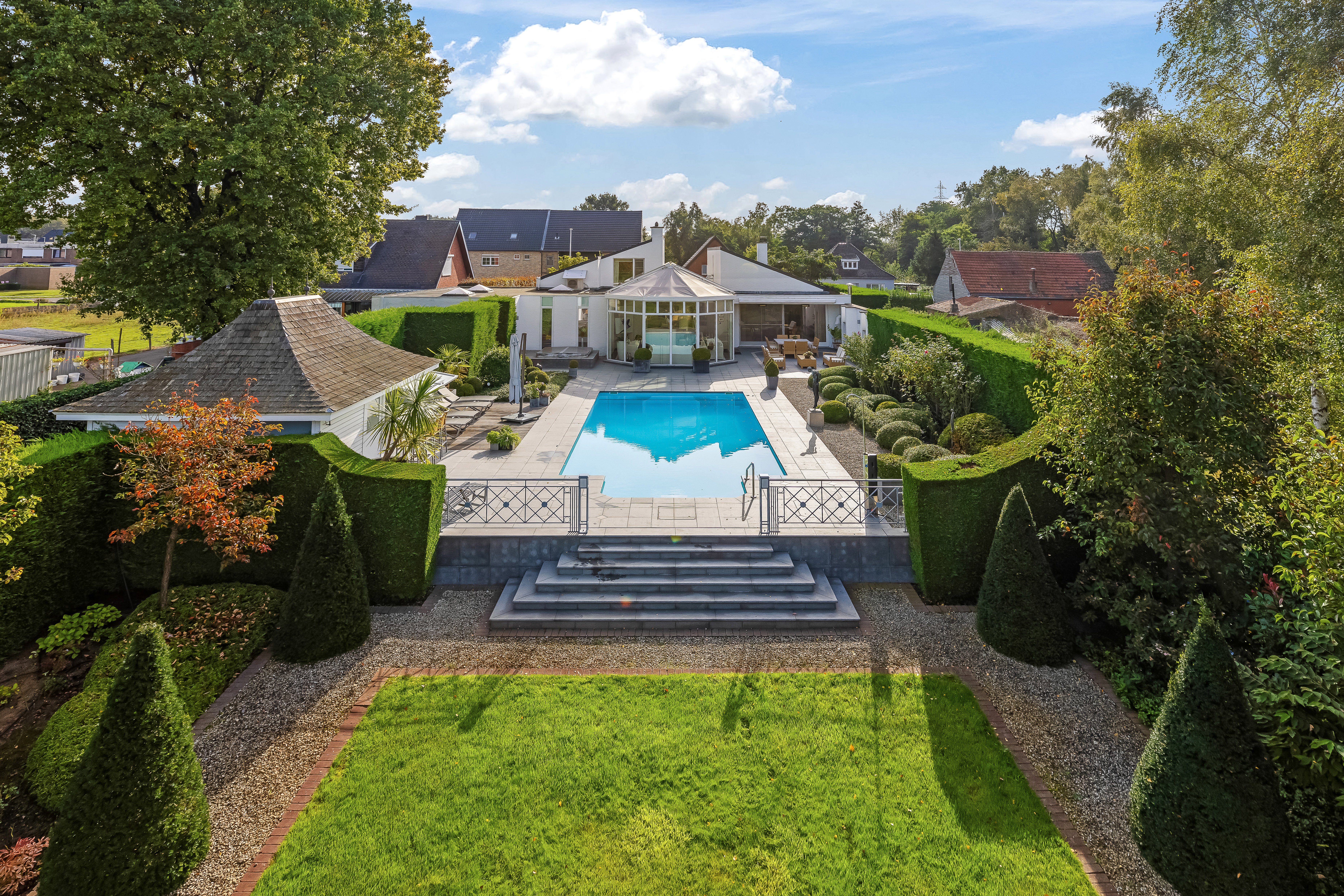 Verhoogd overzicht van een moderne tuin met zwembad en luxe villa, vastgelegd via een hoogtestatief voor een perfecte weergave van de tuinarchitectuur en het perceel.